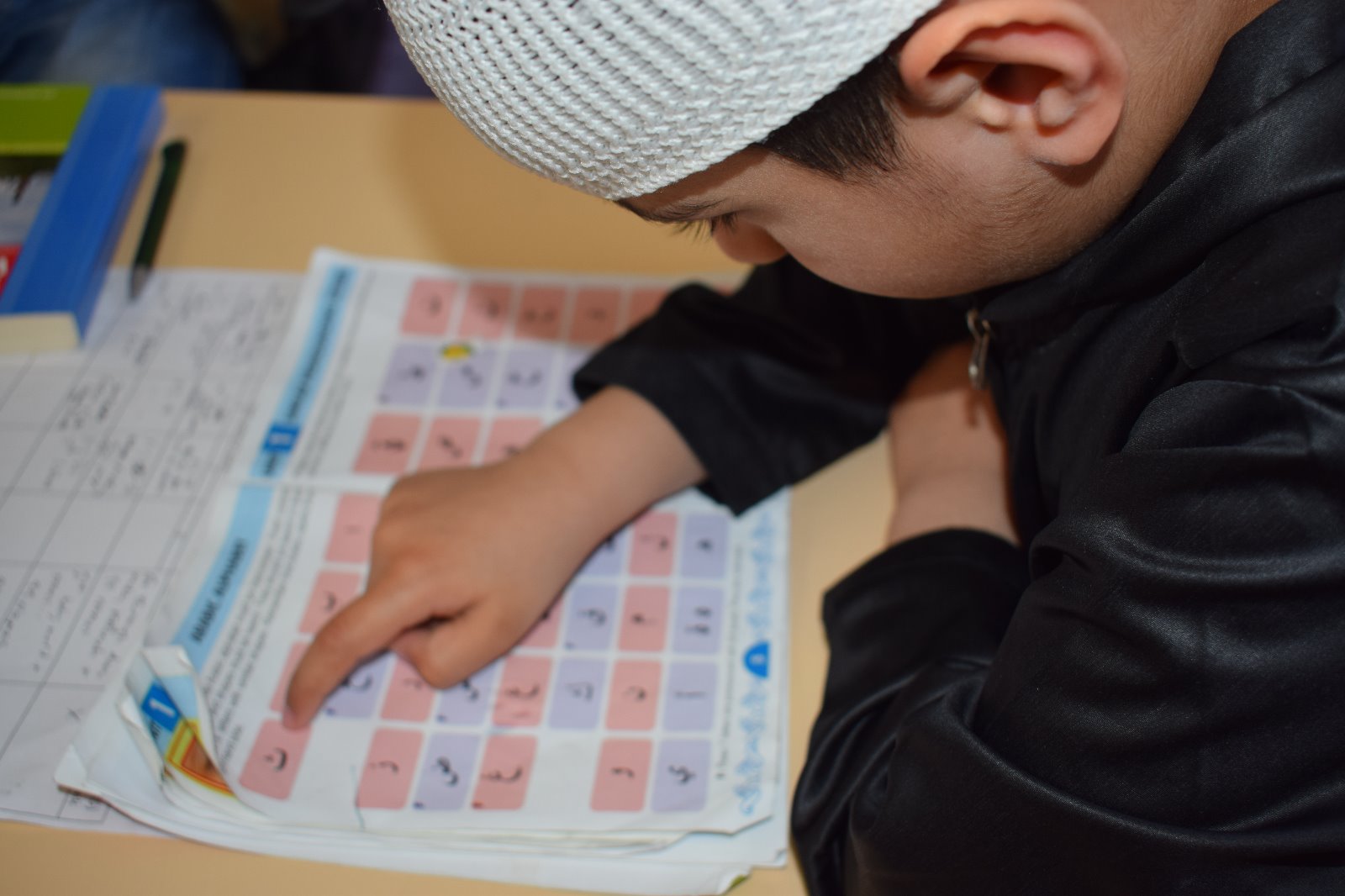 Young pupil tracing letters on a Quran reading page during a lesson